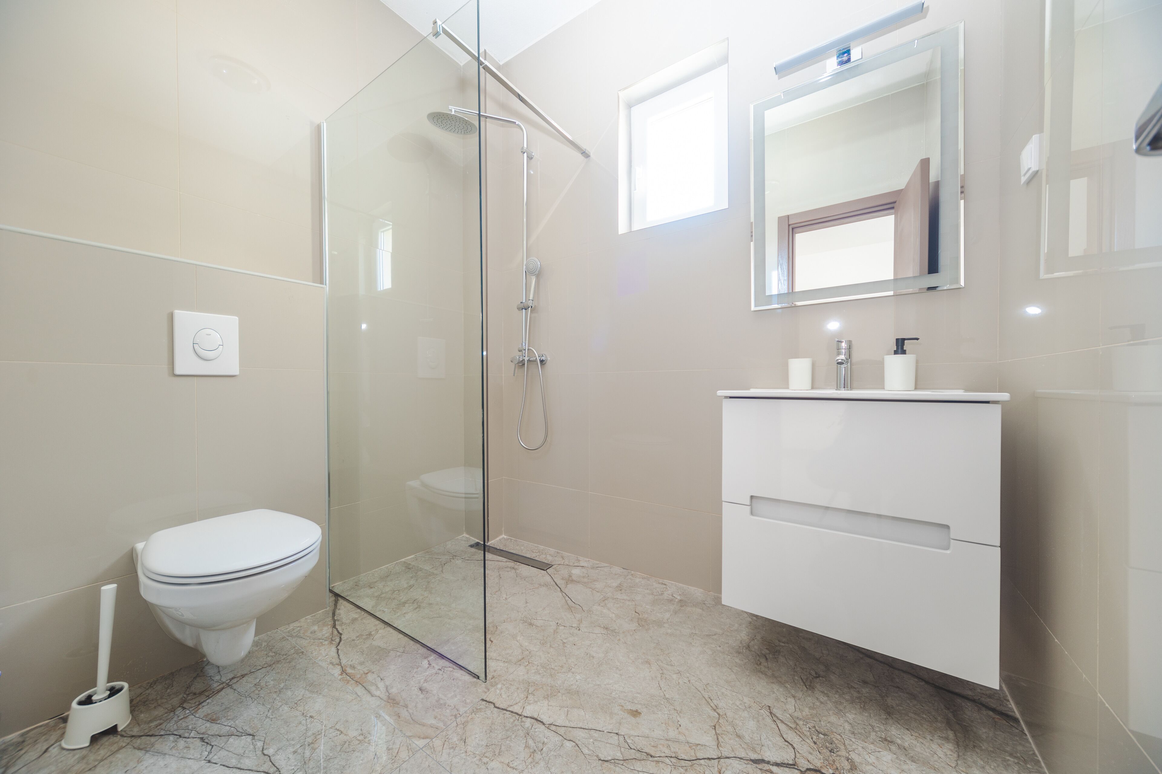 Une salle de bain moderne avec une douche à parois de verre, des toilettes et un meuble-lavabo blanc doté d’un miroir.