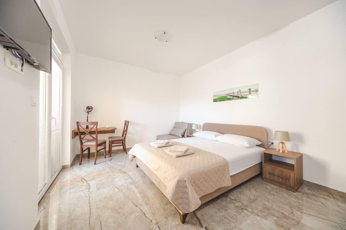 A bedroom with a bed, bedside table, lamp, and a desk with chairs.