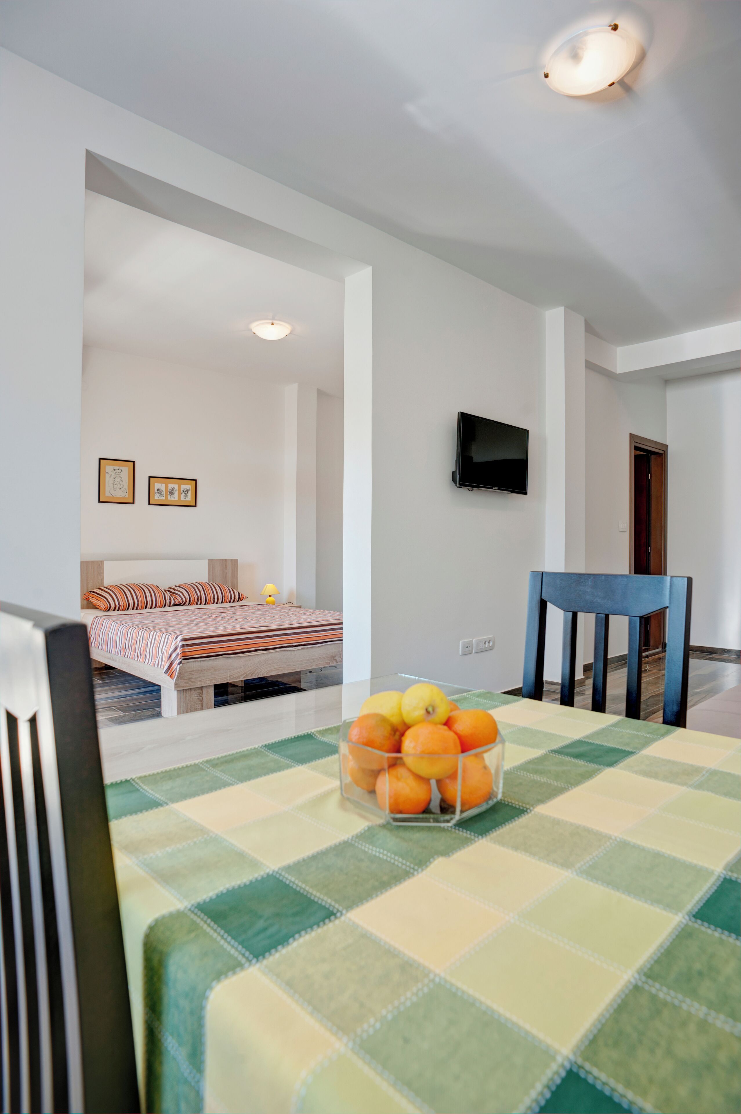 Une chambre avec un lit, un téléviseur fixé au mur et une table sur laquelle se trouve un panier de fruits.