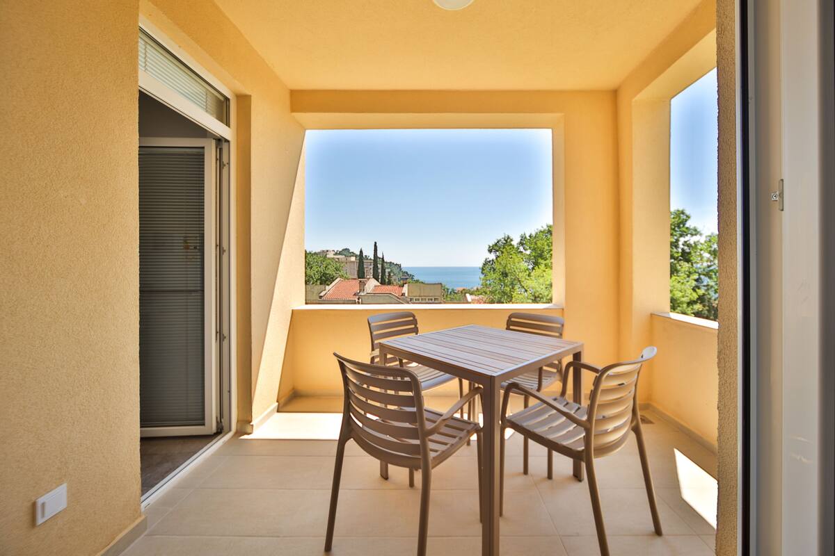 A balcony with a table and chairs, a view of the sea, and a building in the background.