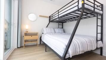En køjeseng med et trænatbord og en lampe, et rundt spejl på væggen og en skydedør i glas.