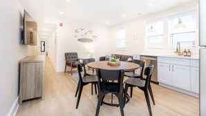 A modern kitchen with white cabinets, a dining area with a round table and chairs, and a visible clock on the wall.