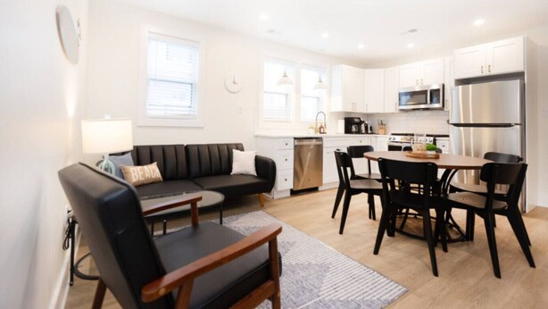 A modern kitchen with white cabinets, stainless steel appliances, and a dining area with a black table and chairs.