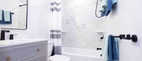 A modern bathroom with a white marble shower, a white toilet, and a vanity with a mirror.