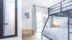 A modern bedroom with a bunk bed, a wooden bench, a bedside table, and a large window offering a view of the outside.