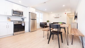 Une cuisine moderne avec des meubles blancs, des appareils en acier inoxydable et une table à manger en bois, assortie de chaises.