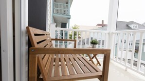 Un banc en bois sur un balcon doté de balustrades blanches, offrant une vue sur les maisons voisines.