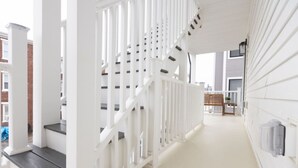 Un escalier blanc avec une rampe, menant à un palier où se trouve un banc.