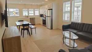 A modern kitchen with white cabinets, a stainless steel refrigerator, and a dining area with a wooden table and chairs. - Steps to THE Beach – 3 BDR Condo + Parking (Wildwood)