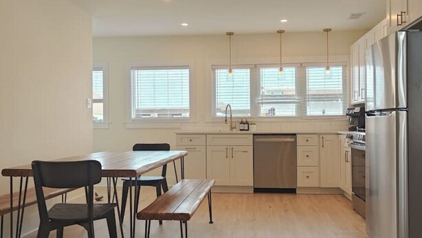 A modern kitchen with white cabinets, stainless steel appliances, and a dining area with a wooden table and chairs. - Steps to THE Beach – 3 BDR Condo + Parking (Wildwood)