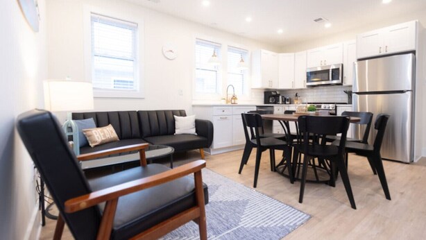A modern kitchen with white cabinets, a stainless steel refrigerator, and a dining area with black chairs and a wooden table. - 500 ft to boardwalk, 3 bdr condo (Wildwood)