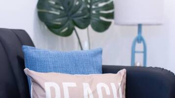 A black sofa with a beige pillow that reads "BEACH" and a blue pillow.
