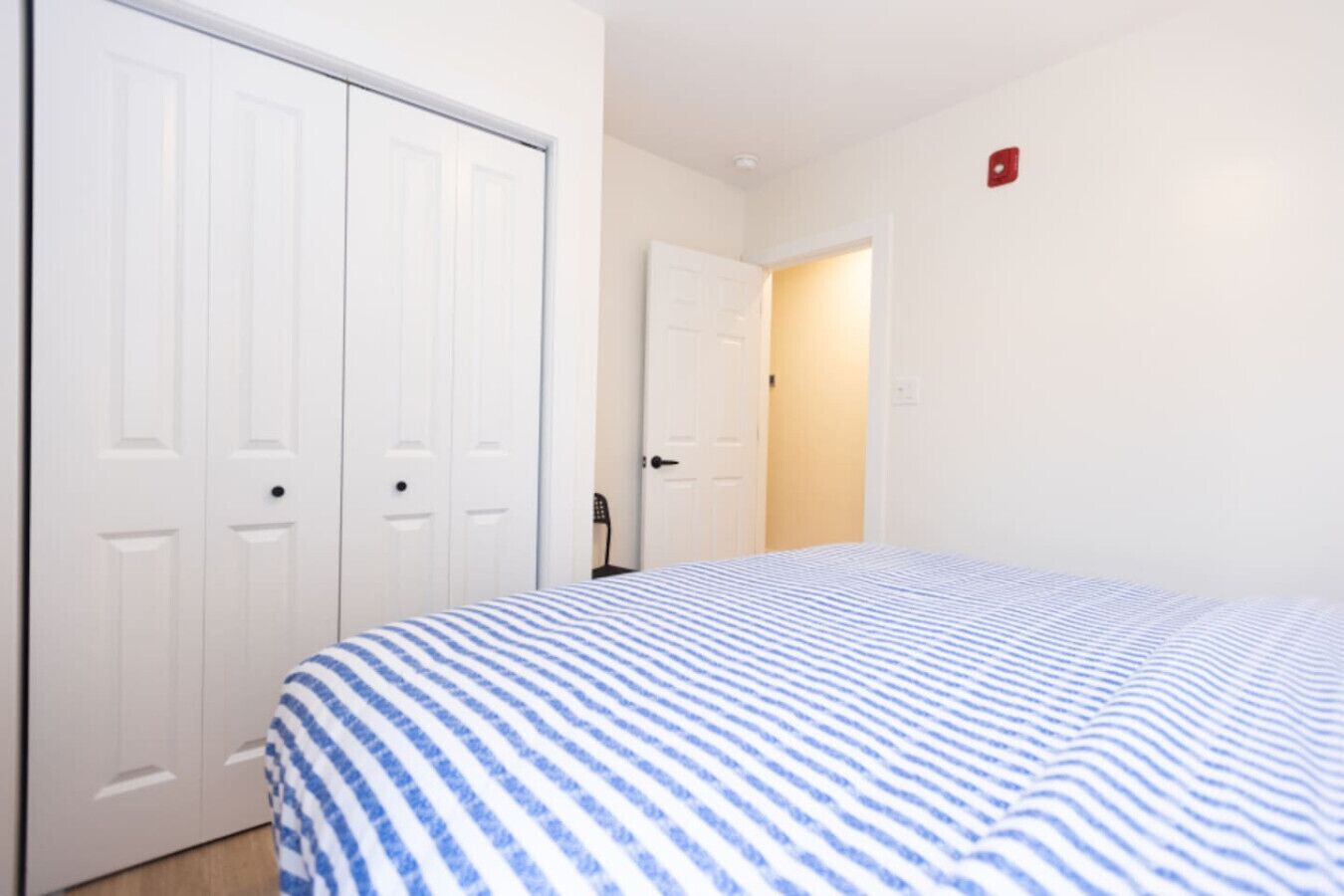 Un dormitorio con cama, dos puertas blancas y una luz de emergencia roja.