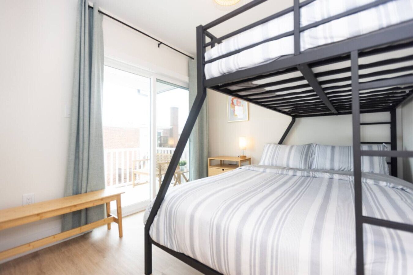 A bunk bed room with a wooden bench, a nightstand, and a window with a view of the outside.