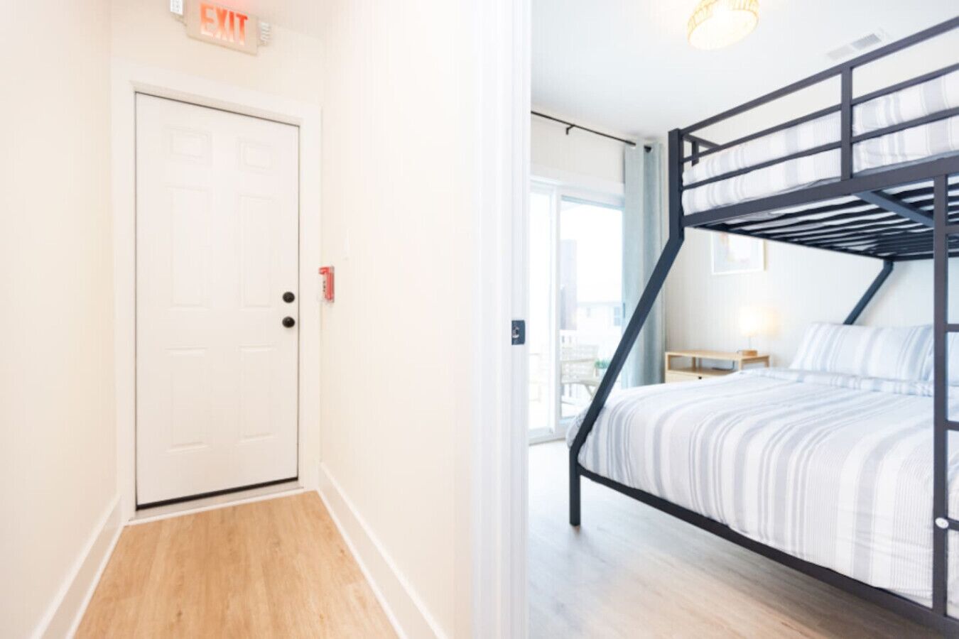 A room with a bunk bed, a white door, and a small table with a lamp.