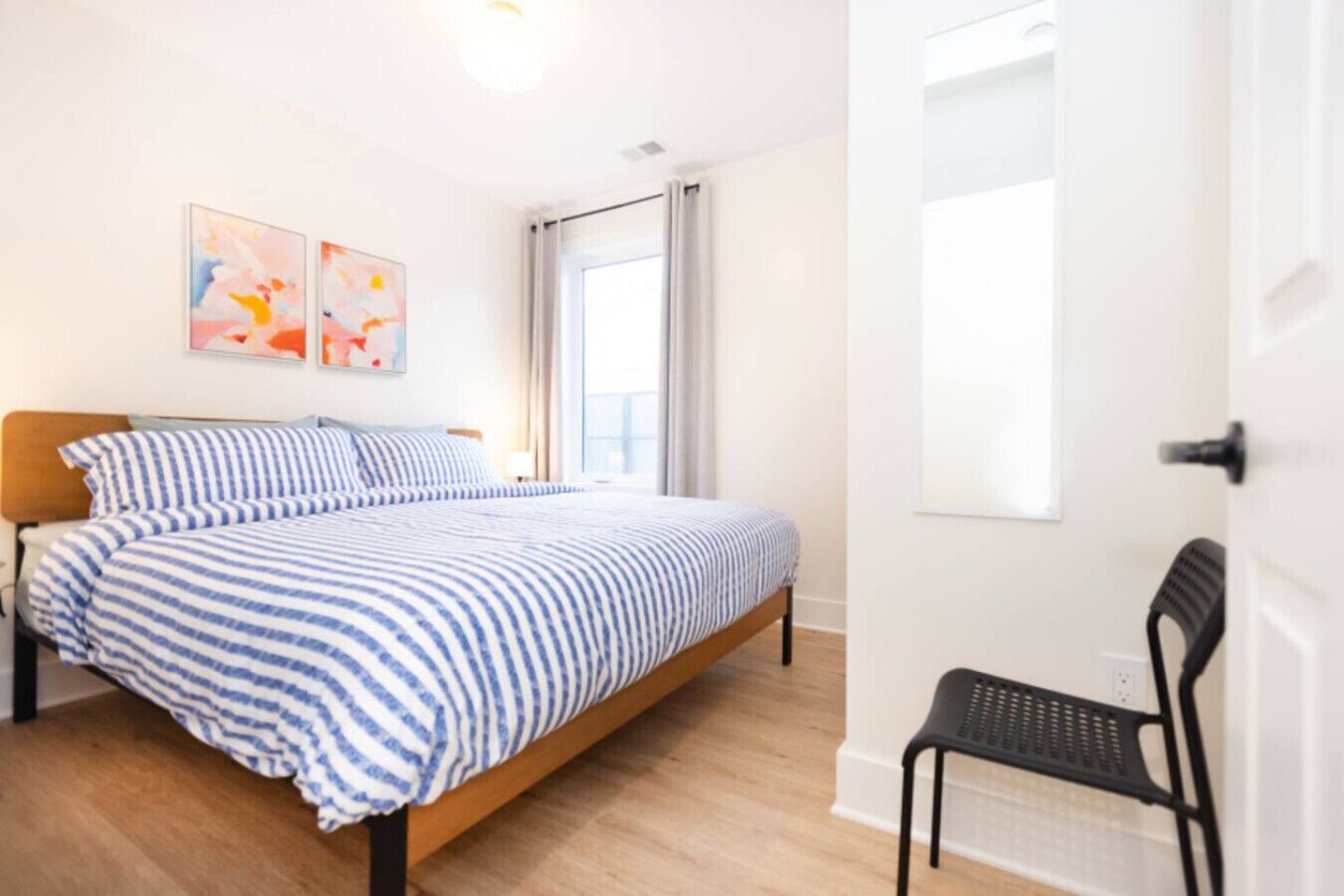 A bedroom with a bed, a chair, and two abstract paintings on the wall.