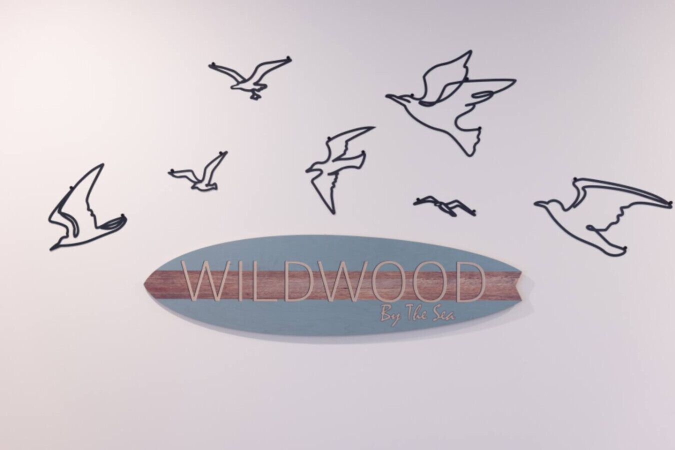 A wooden board with the text "WILDWOOD By The Sea" and outlines of birds flying.