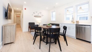 A modern kitchen with white cabinets, a stainless steel dishwasher, and a dining area with a round table and black chairs. - 500 ft to boardwalk, 3 bdr condo (Wildwood)