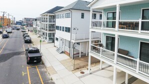 A multi-story residential building with balconies, a parking lot, and a street view. - Amazing all new 1fl condo> Steps to The Beach (Wildwood)