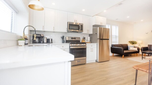 A modern kitchen with white cabinets, stainless steel appliances, and a wooden floor. - Amazing all new 1fl condo> Steps to The Beach (Wildwood)