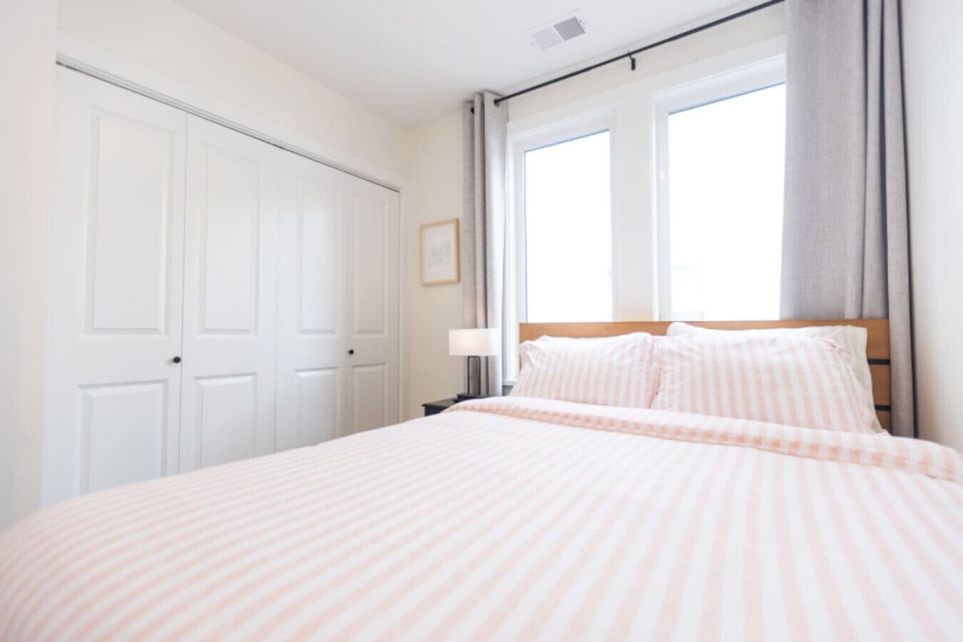 A bedroom with a large bed, a nightstand, a window with curtains, and a white door.