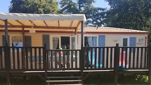 A wooden deck with a covered area, a set of stairs leading up to a door, and a fenced yard. - Spacious mobile home with terrace and lake view, ideal for families. (Bairon et ses environs)