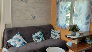 A cozy living area with a dark grey sofa, patterned cushions, a small white side table, and a patterned rug. - Spacious mobile home with terrace and lake view, ideal for families. (Bairon et ses environs)
