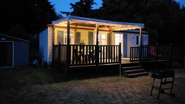A small, single-story cabin with a porch and a covered deck area, surrounded by trees and a grassy yard. - Spacious mobile home with terrace and lake view, ideal for families. (Bairon et ses environs)