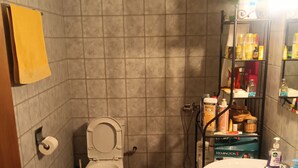 Une salle de bain comprenant des toilettes, un lavabo et une douche. On y trouve une étagère avec des articles de toilette et un porte-serviettes.