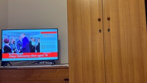 Une pièce avec une armoire en bois et un téléviseur diffusant un journal télévisé.