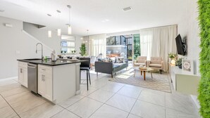 A modern kitchen with a central island, dining area with a sofa and chairs, and a living room with a sofa and coffee table.