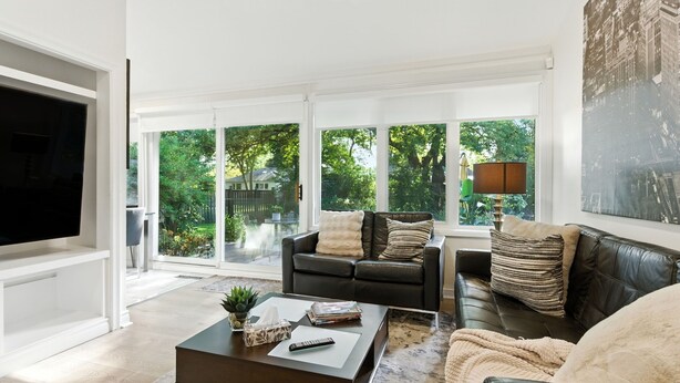 A modern living room with a large flat-screen TV, a dark leather sofa, and a coffee table with remote controls and magazines.
