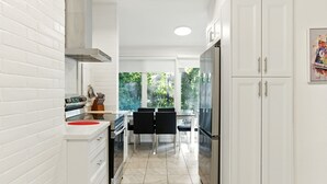 A modern kitchen with white cabinetry, a dining area with black chairs, and a large window offering a view of greenery.