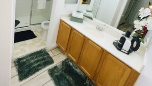 A bathroom with a glass shower enclosure, a white sink, wooden cabinets, and a large mirror with lights above it. - Charming studio in soothing North Las Vegas with AC (North Las Vegas)