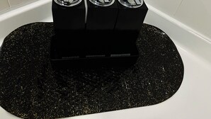 A black, glittery mat with three black containers labeled "SHAMPOO," "CONDITIONER," and "BODY WASH" in a bathroom. - Charming studio in soothing North Las Vegas with AC (North Las Vegas)