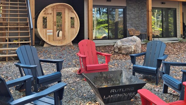 A modern house with a stone facade, large windows, and a deck with Adirondack chairs. - Newly constructed, beautiful, modern lakehouse with new barrel sauna  (Mactier)
