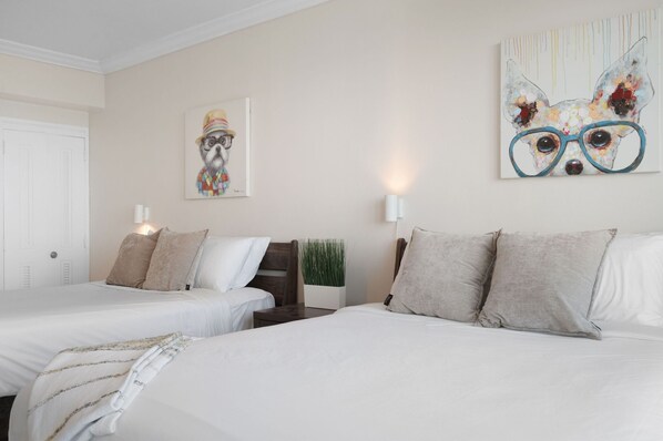 A hotel room with two beds, a nightstand, a wall-mounted lamp, and a painting of a dog wearing glasses.
