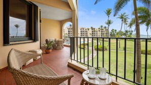 A balcony with wicker furniture, a view of a pool, and palm trees. - Beachfront Paradise 2BR Crescent Beach Seaside (Humacao)