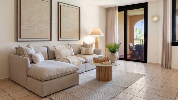 A modern living room with a beige sectional sofa, a round wooden coffee table, and two framed artworks on the wall. - Beachfront Paradise 2BR Crescent Beach Seaside (Humacao)
