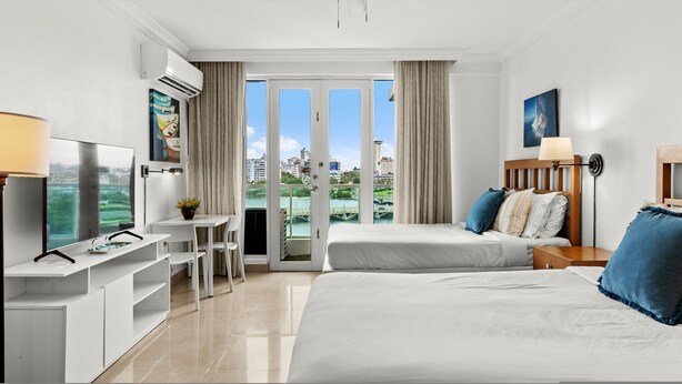 Une chambre d’hôtel comprenant un lit, un bureau avec une télévision, une chaise et un balcon avec vue sur la ville.