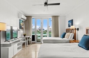 Camera d'albergo con un letto, una scrivania con televisore, una sedia e un balcone con vista sulla città.