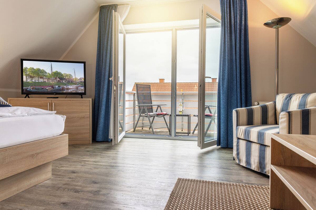 Ein Hotelzimmer mit Bett, Fernseher, Sofa, Balkon mit Blick auf Gebäude und einer Stehlampe.