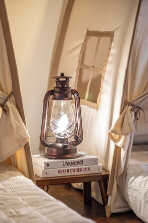 Een gezellige tent met een lantaarn op een tafel, een boek getiteld 'Onbekende Kathedralen' en een bed met een witte dekbedovertrek.