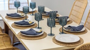 Una mesa de comedor dispuesta con servilletas azules, platos blancos y cristalería transparente.