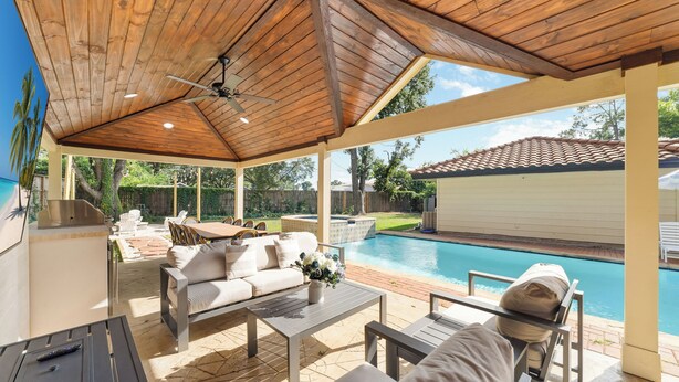 Un patio cubierto con piscina, mobiliario exterior y ventilador de techo.