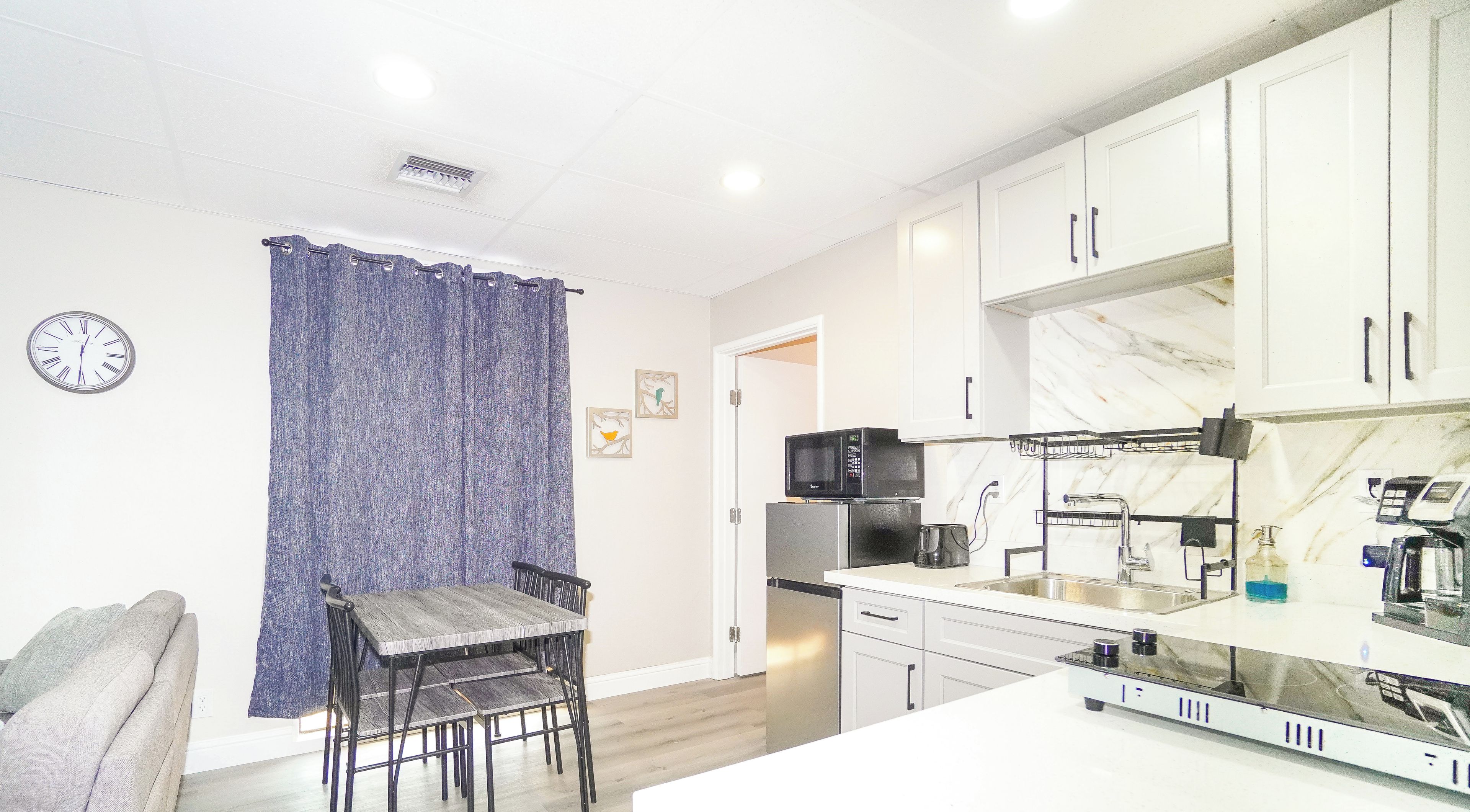 A modern kitchen with white cabinets, a built-in microwave, and a dining area with a table and chairs.