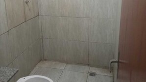 Une petite salle de bain carrelée, équipée de toilettes et d’un espace douche.