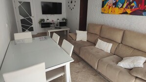 Ein modernes Wohnzimmer mit einem beigefarbenen Sofa, einem weißen Esstisch und einem Deckenventilator.