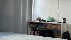 Hotellihuone, jossa on sänky, seinälle asennettu televisio, työpöytä, jossa on erilaisia tavaroita, ja matkalaukku.