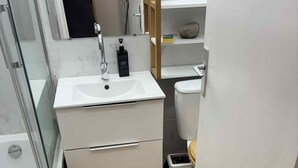 Un baño pequeño y funcional con lavamanos blanco, espejo, inodoro y un pequeño cubo de basura.